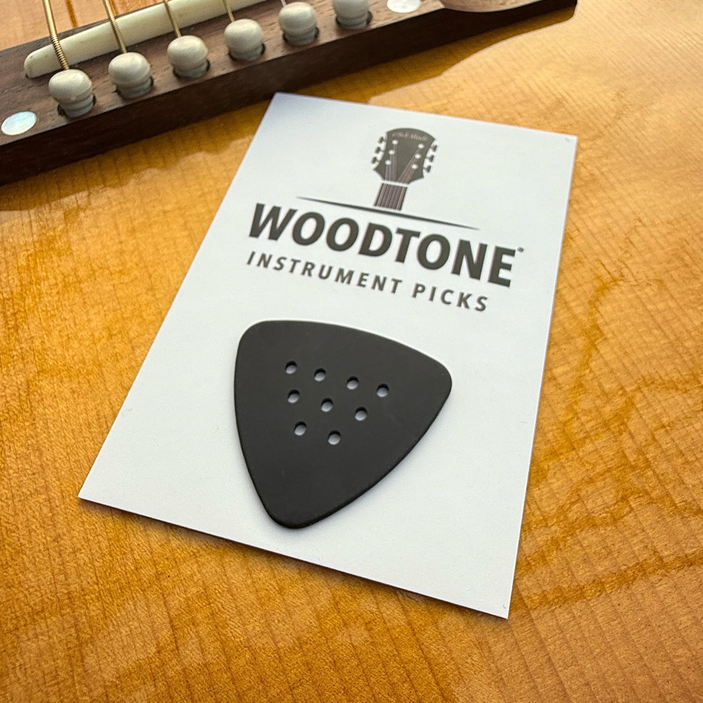 Black guitar pick on a Woodtone Instrument Picks card with a guitar in the background